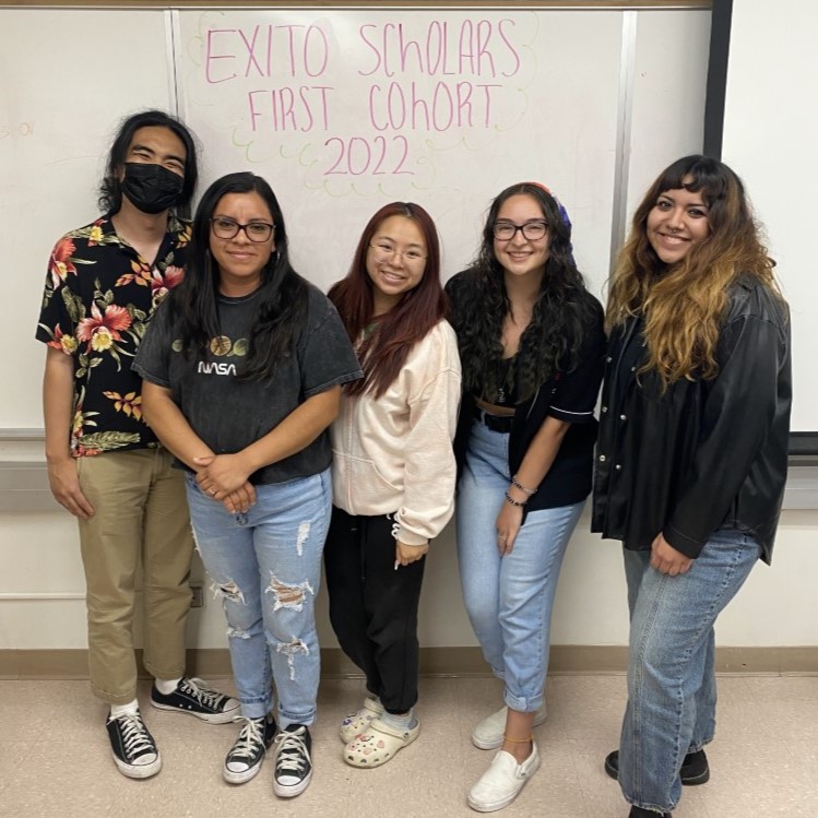 "Five students who make up the first cohort of EXITO scholars from 2022 stand in front of a whiteboard"