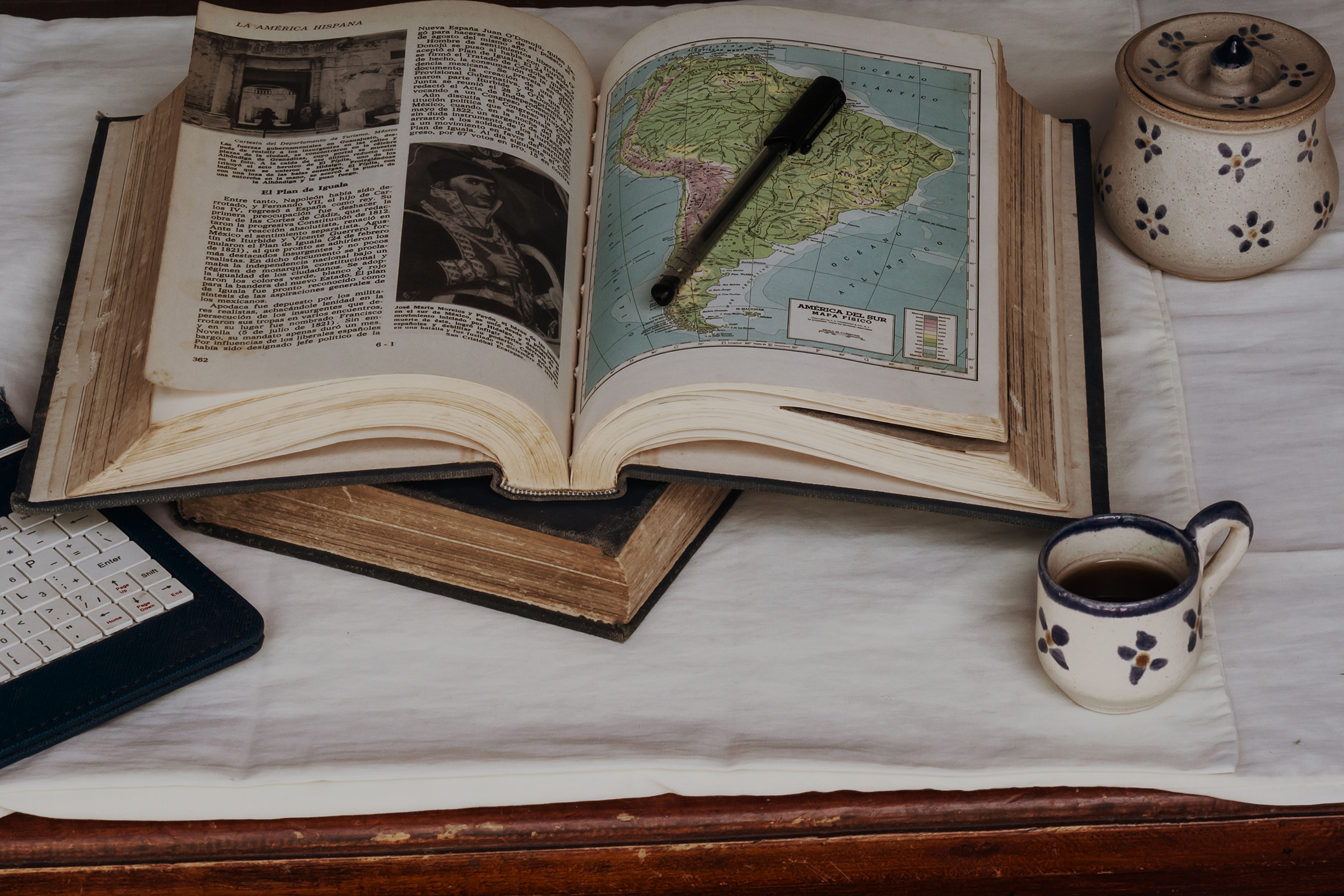 Book opened on South America map with pen on top and small coffee cup next to it